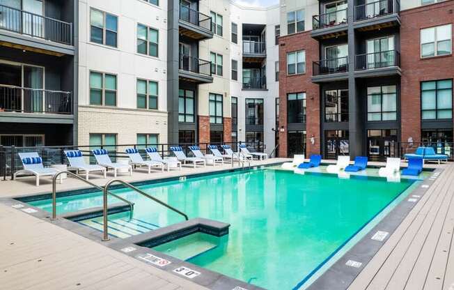 A pool surrounded by chairs and buildings.
