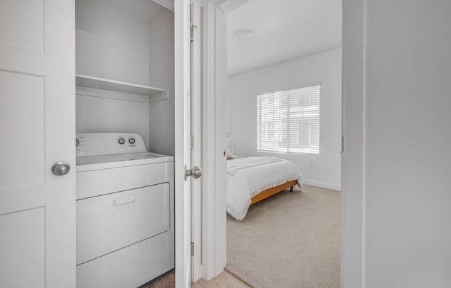 a laundry room with a washer and dryer and a bed in the background