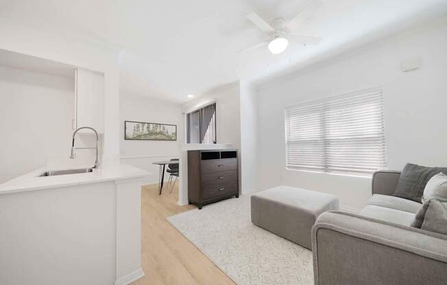 A modern living room with a grey couch and a white kitchen area.