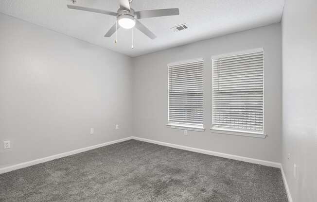 an empty room with a ceiling fan and two windows