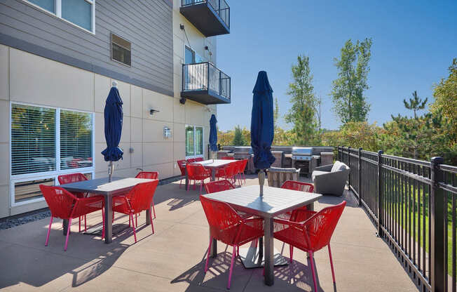 A patio with red chairs and tables is surrounded by a black fence.