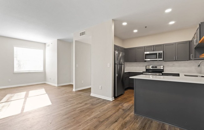 an empty living room with a kitchen with stainless steel appliances at Switchback on Platte Apartments, Littleton, CO 80120