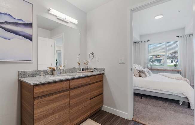 a bathroom with a vanity and a mirror and a bedroom with a bed