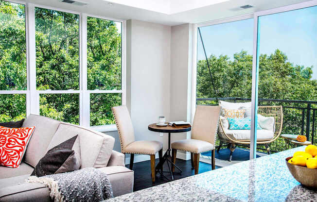 An elegant living room with luxurious stain-resistant plank flooring, a gas fireplace, and expansive windows that offer picturesque views of nature. A seamless transition to a balcony creates a spacious indoor-outdoor connection.