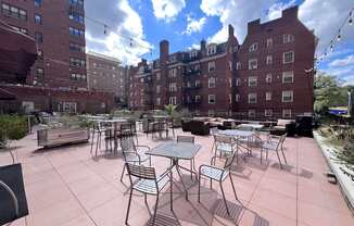 A patio with tables and chairs is surrounded by brick buildings.
