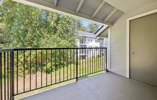 A balcony with a black railing and a view of a green lawn and trees.