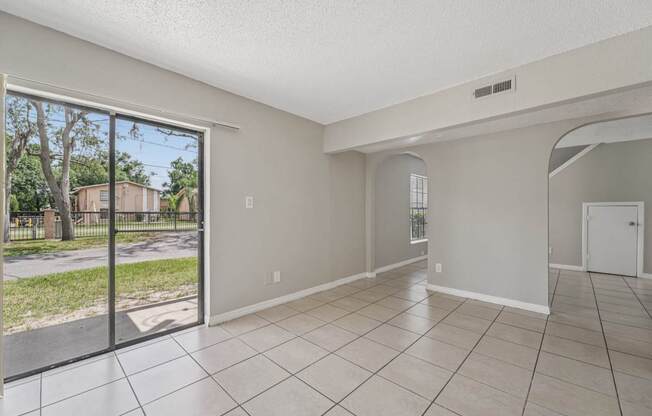A spacious room with tiled flooring and a view of a street through a sliding glass door.