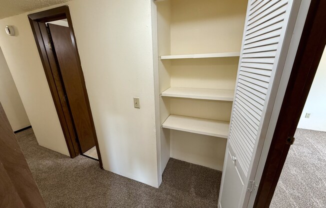 A white closet with three shelves is open.