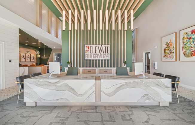 A reception area with a white reception desk and a green wall with a sign that says "Elevate Riverview".