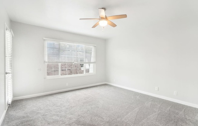 A room with a ceiling fan and a window with blinds.