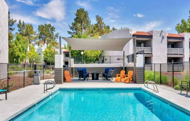 A swimming pool in front of a building with orange chairs around it.