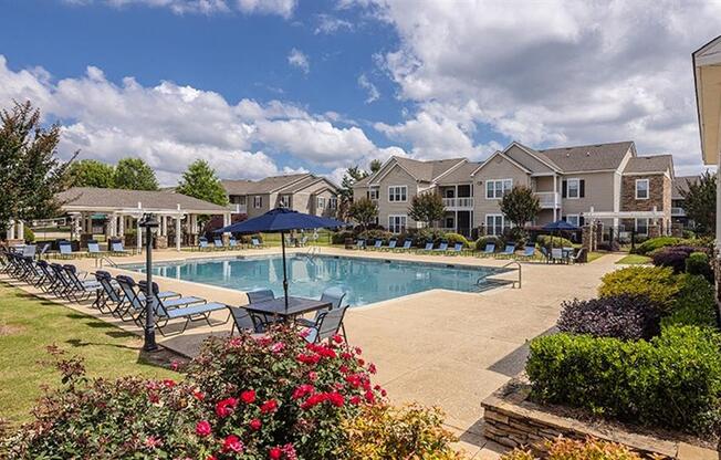 a swimming pool with chairs and umbrellas in front of houses at Bedford Parke Apartments, Warner Robins, GA