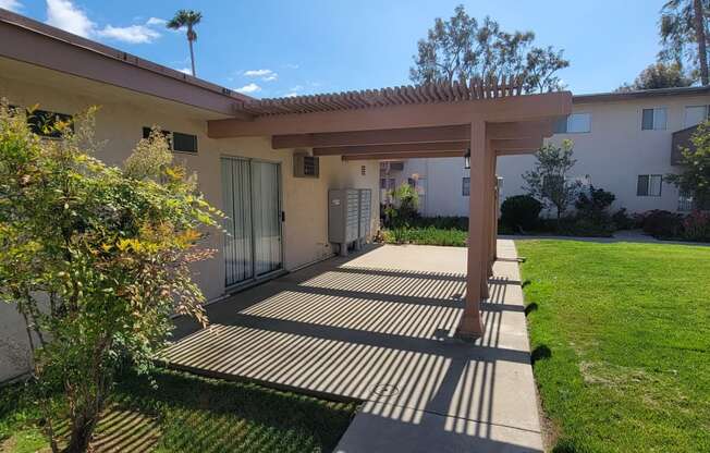 Patio with pergola and mailboxes in grassy courtyard at Plaza Verde Apartments in Escondido, California.