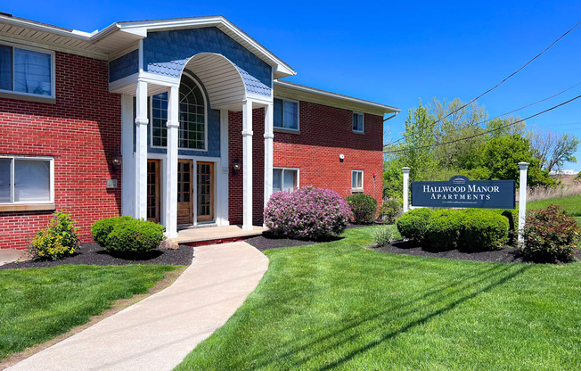 A red brick building with a sign that says "Hallwood Manor Apartments" in front of it.