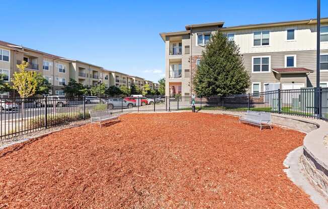 a fenced in dog park in front of an apartment building