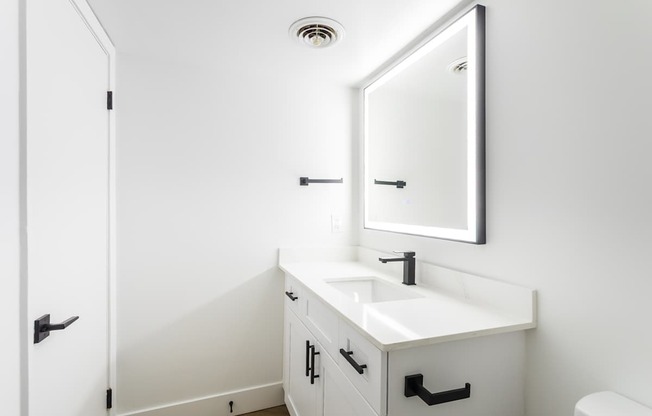 A white bathroom with a sink, mirror, and toilet.
