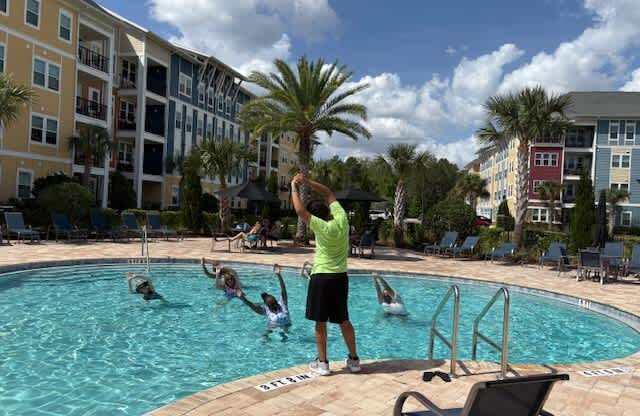 A man in a green shirt is standing by a pool with people swimming.