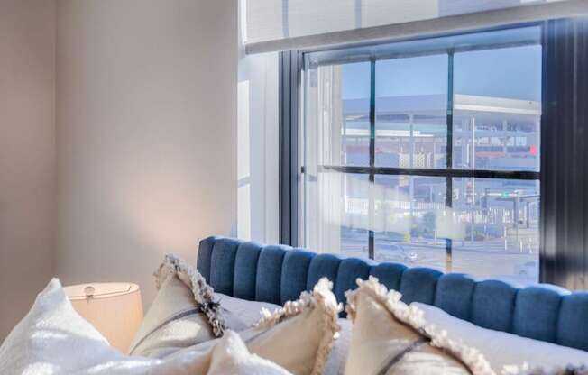 A blue couch with white pillows in front of a large window.