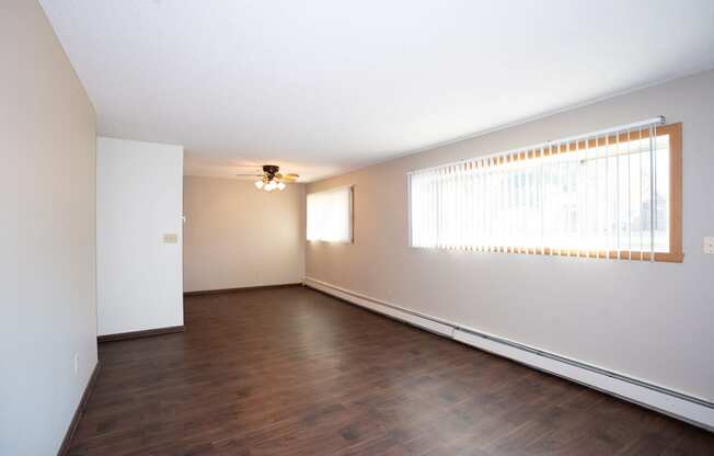 an empty living room with wood floors and a large window. Fargo, ND Country Club Apartments