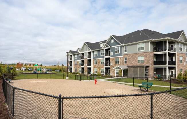 a fenced in dog park with a fire hydrant and benches in front of an apartment