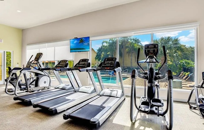 a gym with cardio equipment and a large window with a view of the pool