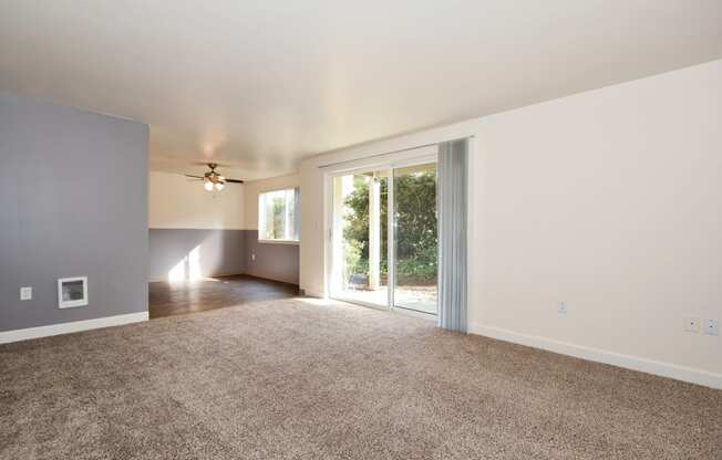 an empty living room with a sliding glass door and a ceiling fan