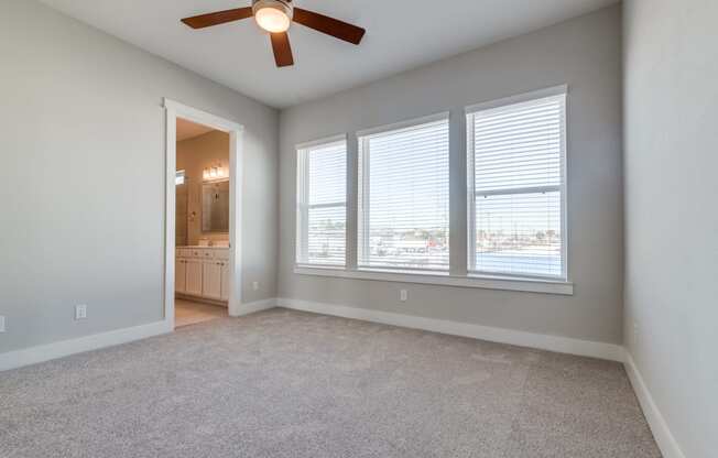 Luxury Three-Bedroom Homes for Rent in Houston, TX - East Heights - Carpeted Bedroom with Large Windows, Soft Grey Walls, Attached Bathroom, and Ceiling Fan.