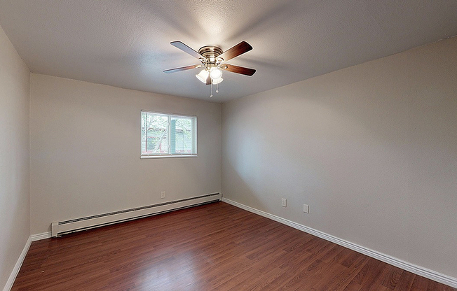 Bright and airy room featuring sleek hardwood flooring, a modern ceiling fan, and a large window letting in natural light.