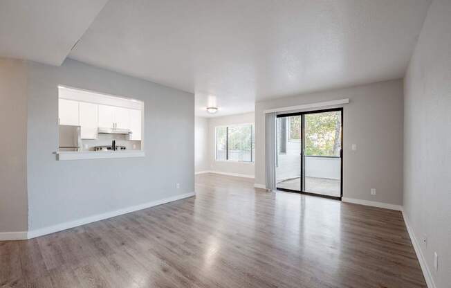 A spacious room with wooden flooring and a sliding glass door leading to a balcony.