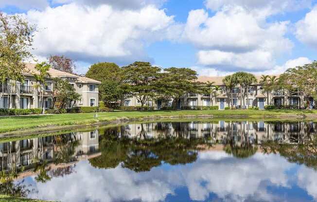 A serene lake in front of a row of houses with trees in the background.