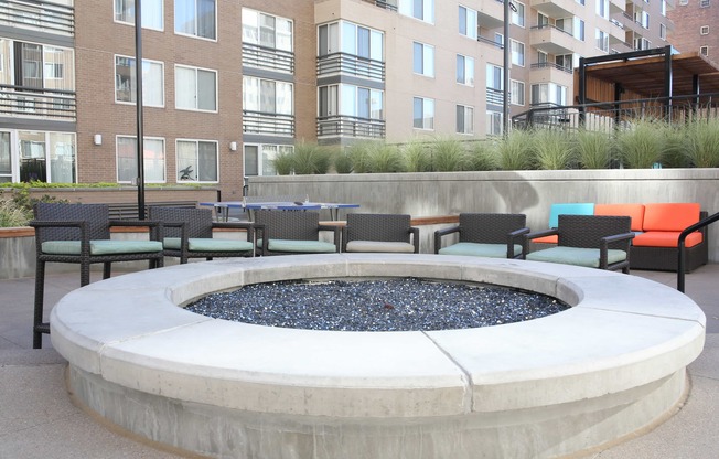 an outdoor seating area with chairs and a fire pit in front of an apartment building