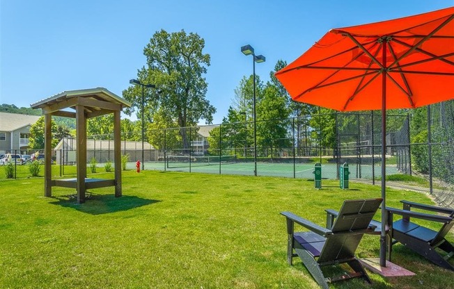 two benches and an umbrella in the grass near a tennis court