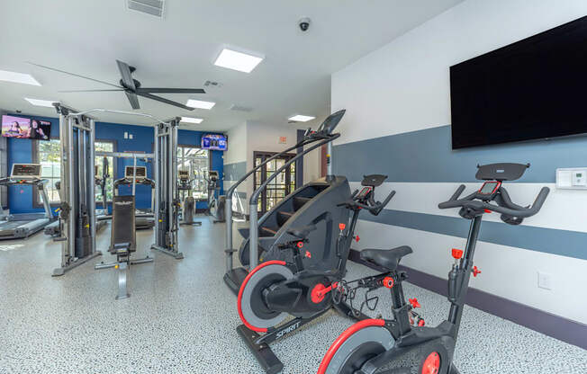 A gym with exercise equipment and a television on the wall.