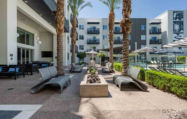 a patio with lounge chairs and a fire pit in front of a slate scottsdale apartment building