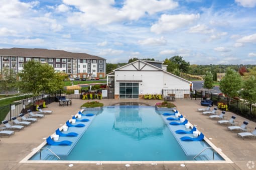 an aerial view of an outdoor swimming pool with blue lounge chairs and a resort building