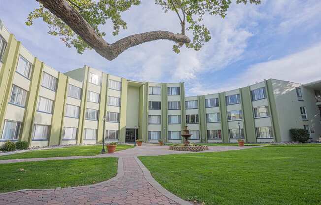 a courtyard in front of an apartment building with green grass and a tree