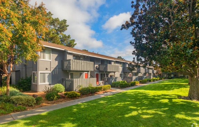 Apartment complex with green grass and trees in front.
