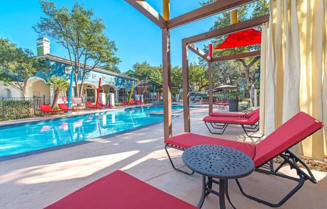A pool area with red lounge chairs and a table at Reserve at Canyon Creek,Texas
