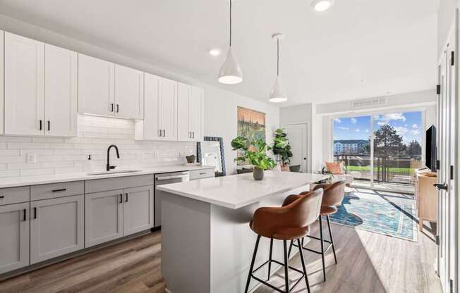 A kitchen with white cabinets and a white island with brown chairs.