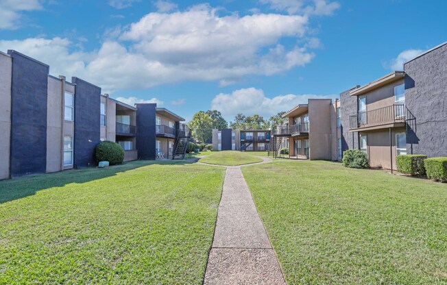 A row of modern apartment buildings with a sidewalk in the foreground at The Drake in Bossier City, LA