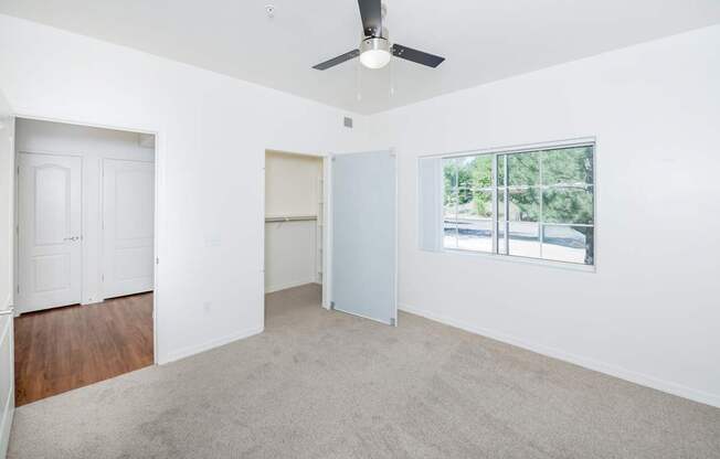 A room with a ceiling fan and a window overlooking a street.