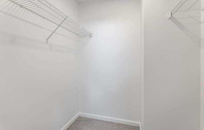 A white closet with a carpeted floor and two metal racks.