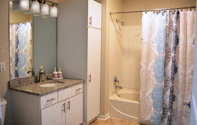bathroom with white vanity, white cabinet and tub with shower curtain partially open at Residences at Forest Park, Missouri