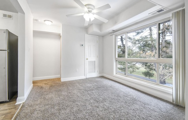 A spacious room with a ceiling fan and a large window overlooking a tree-filled area.