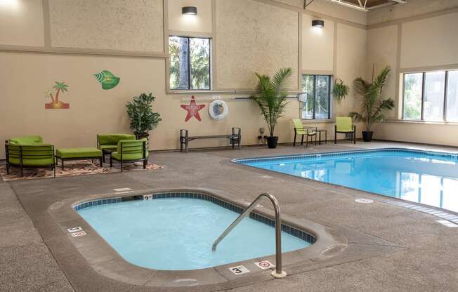 a swimming pool with a hot tub in the middle of a room with green chairs and plants