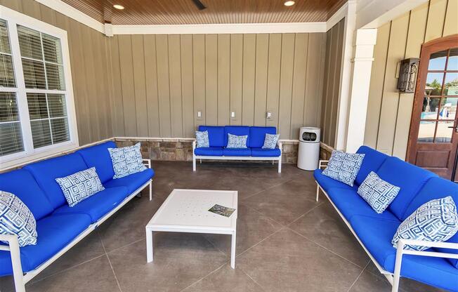 Three cushioned benches and a small table under a ceiling fan on the outdoor covered clubhouse patio