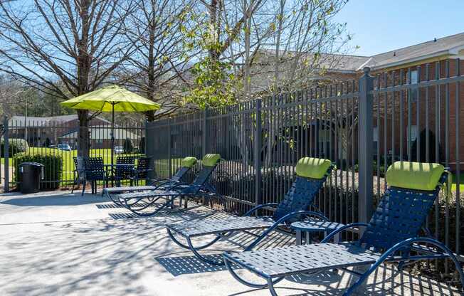 A row of blue lawn chairs with green cushions are lined up on a patio.
