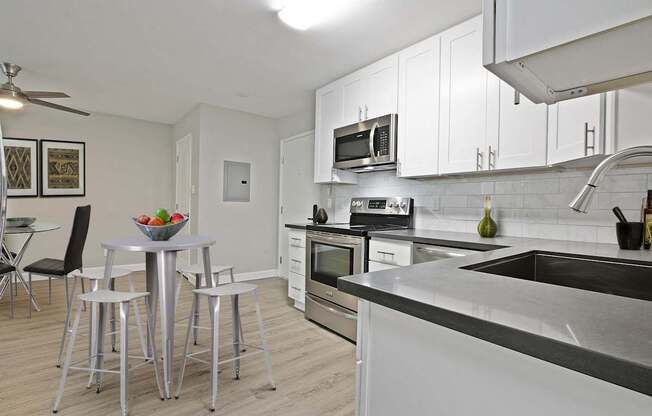 Open kitchen with stainless steel electric stove with micro hood microwave, tile backsplash, white kitchen cabinets, gray quartz counters