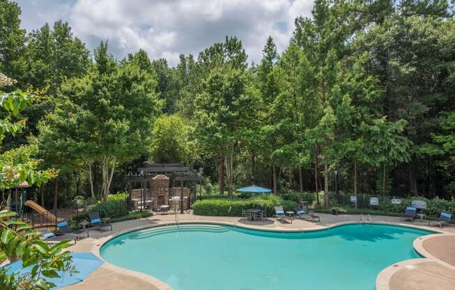 a swimming pool with chairs around it and trees in the background