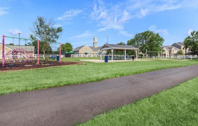 a paved path leading to a park with a playground and a pavilion